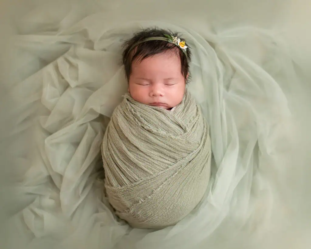 Søt nyfødtbaby sovende innpakket i mykt stoff, omgitt av kremfargede stoffer.