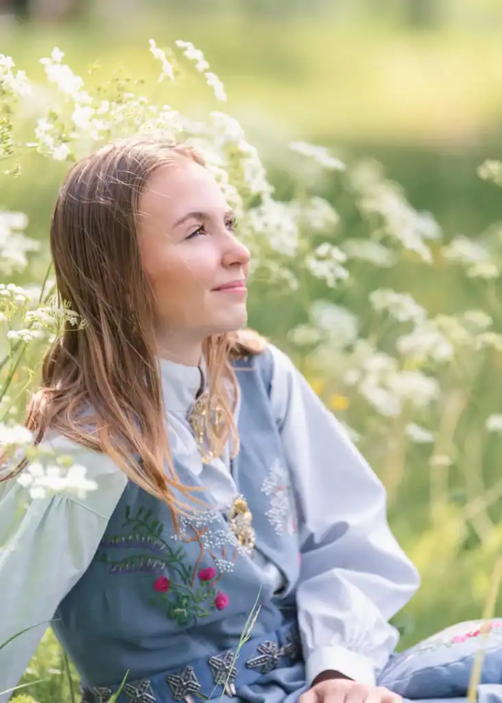Konfirmant i blomstereng med solskinn og grønt landskap.