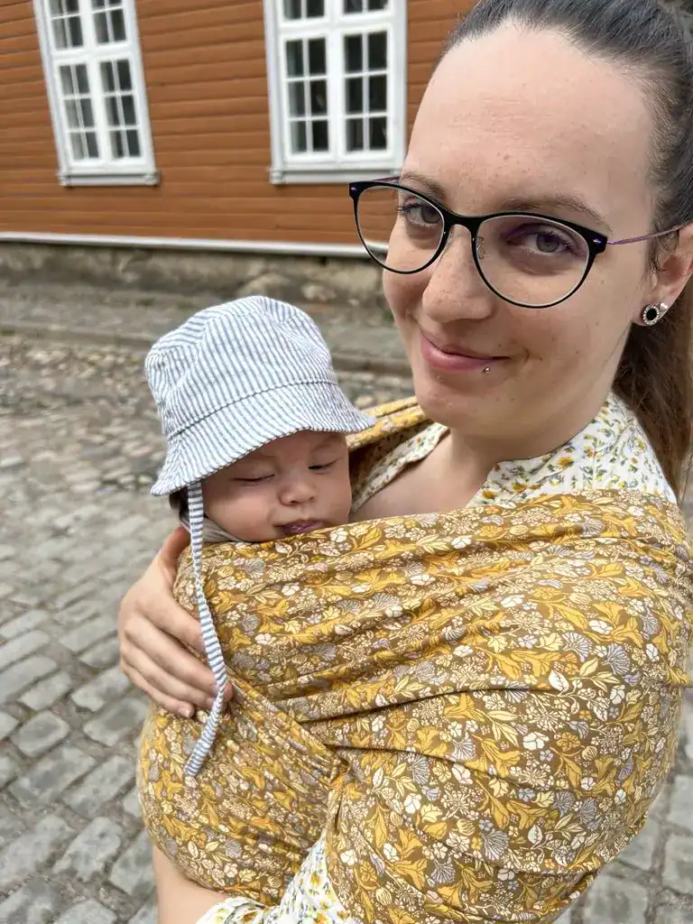 Bæresjal med baby, brukt av mor, i en urban utendørs setting.
