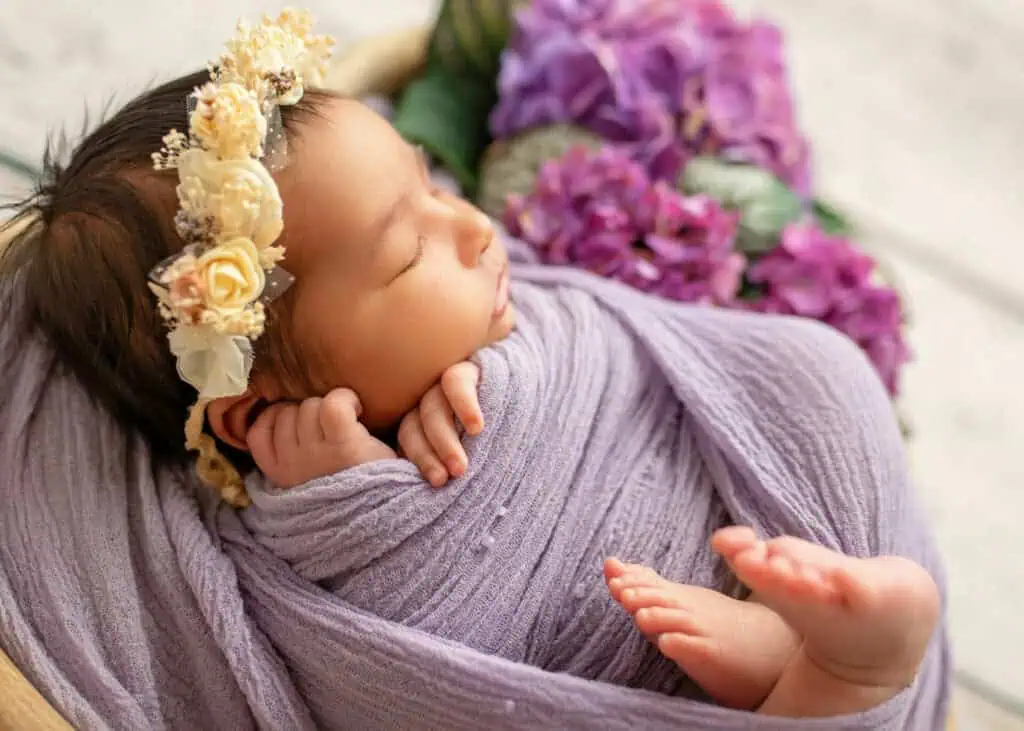 Nyfødt baby med blomsterkrans sover i lilla teppe – nyfødtfotograf Jessheim