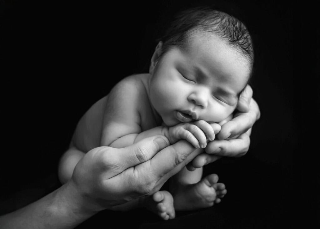 Nyfødt baby sover i hendene til en voksen – svart-hvitt – nyfødtfotograf Oslo