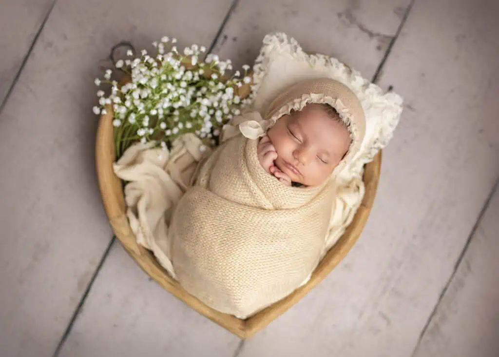 Nyfødt jente i hjerteskål med blomster på nyfødtfotografering