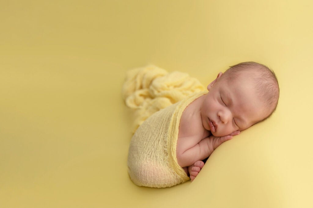 Nyfødtbaby sovende på myk gul bakgrunn, fotografert i Oslo.