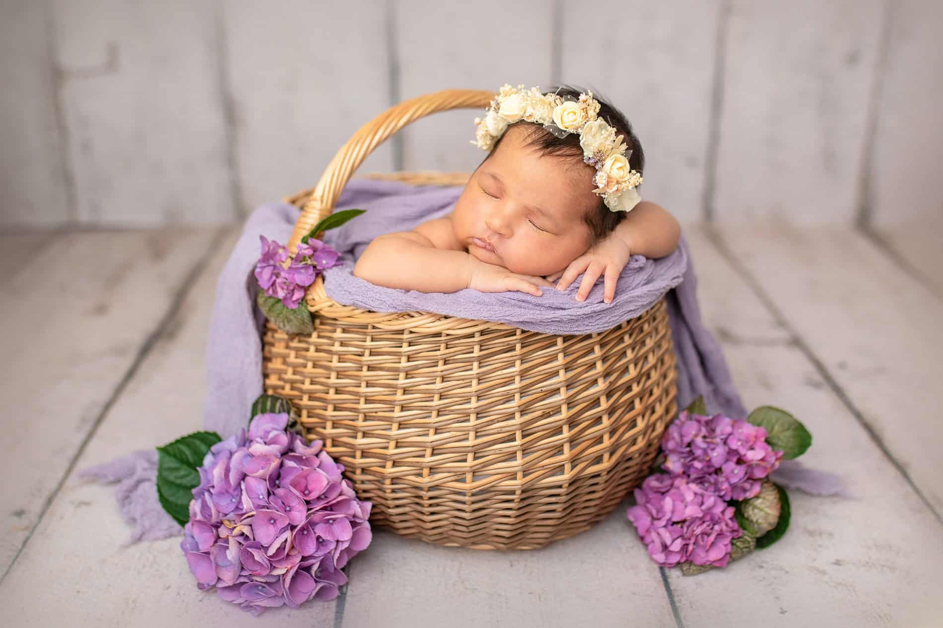 Søt baby sover i kurv med blomster og blomsterkrans, fotografert i Oslo.