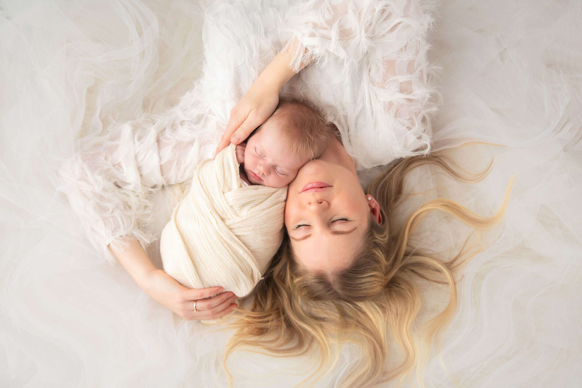 Søvnende nyfødtbarn fotografert under nyfødtfotografering, med myke tekstiler og naturlig lys.